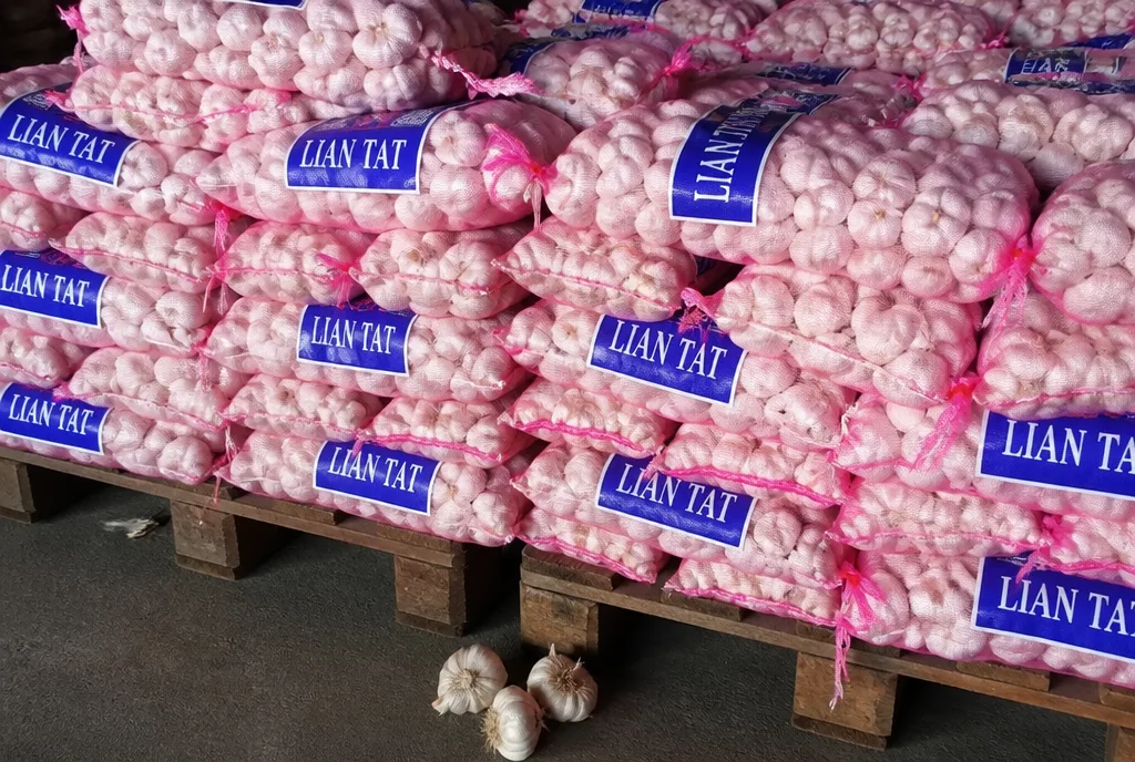Mesh bags of whole garlic stacked on a pallet with Lian Tat tags