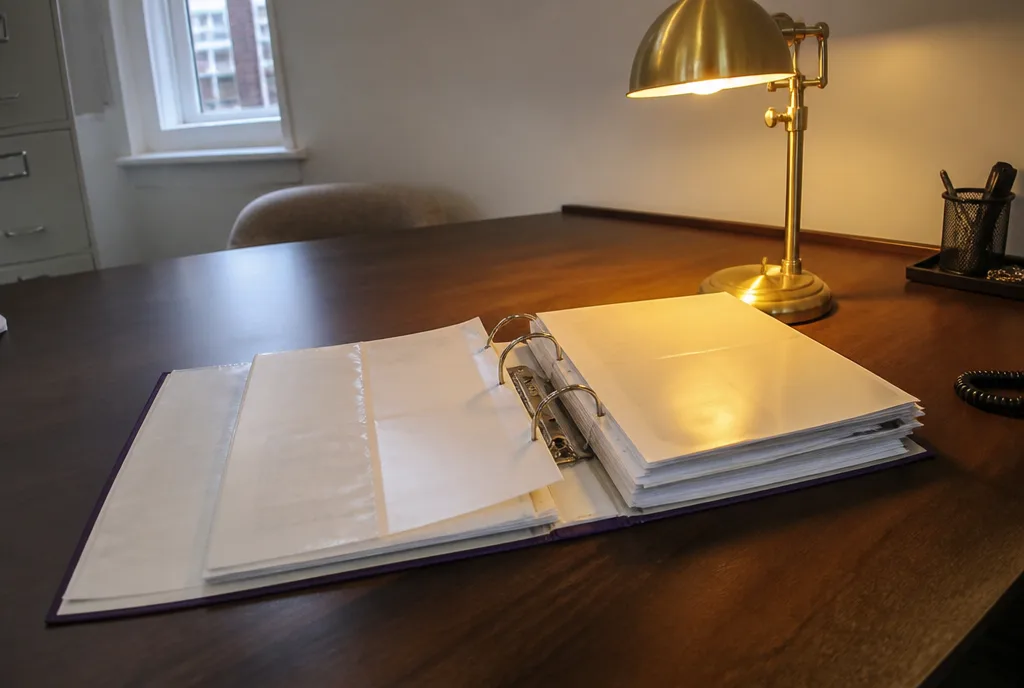 An open ring binder of completed transaction files on a desk with a lamp