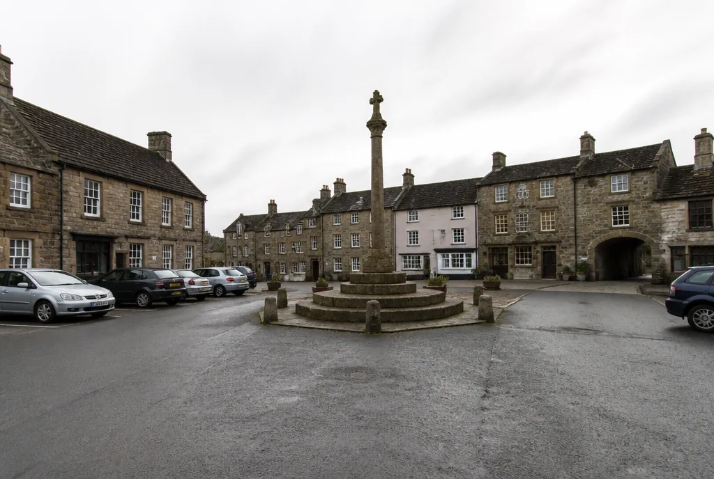 The market place in Oakham with stone buildings and a butter cross under an overcast sky