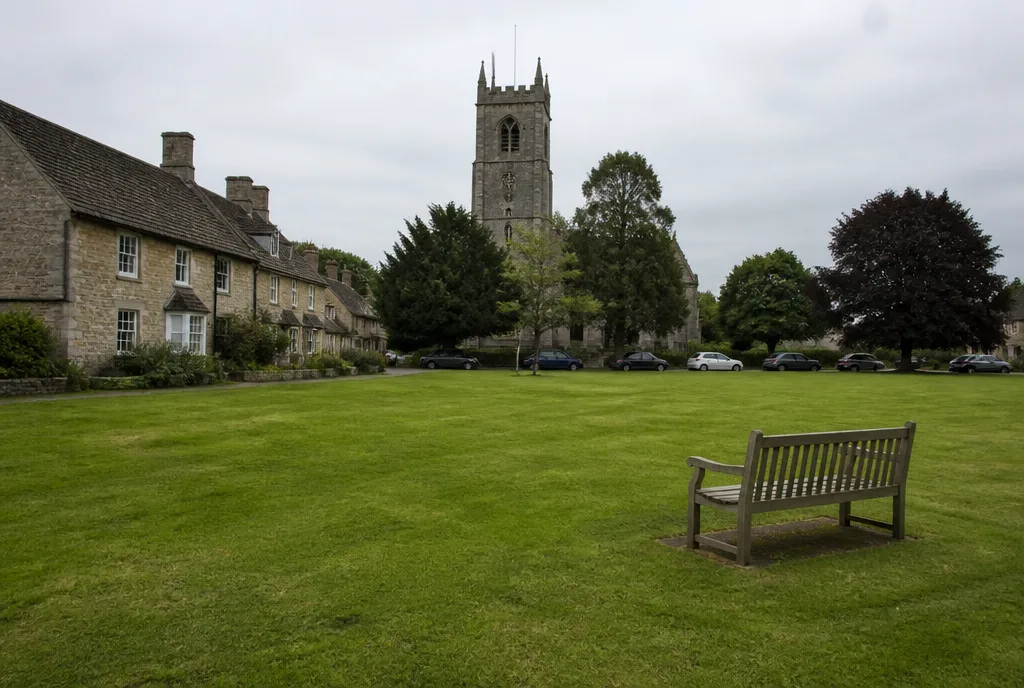 A village green with a stone church tower and parked cars at Ryhall on a grey day