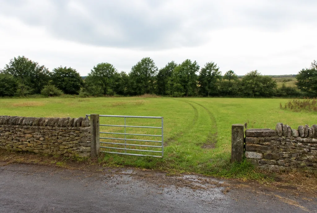 An empty grassed development plot behind a stone wall with a gate and open countryside beyond