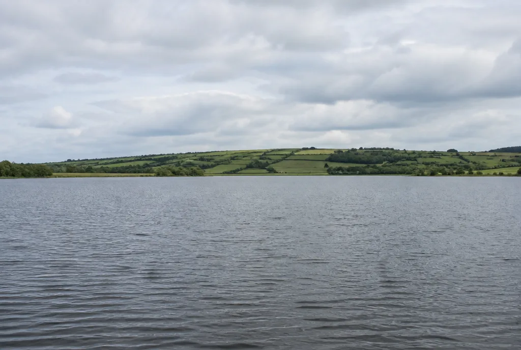 A wide view over open water with low green hills and a pale sky beyond