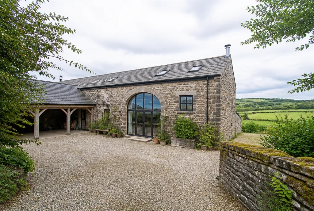 A converted stone barn with a huge glazed cart-arch window, gravel courtyard and open countryside behind