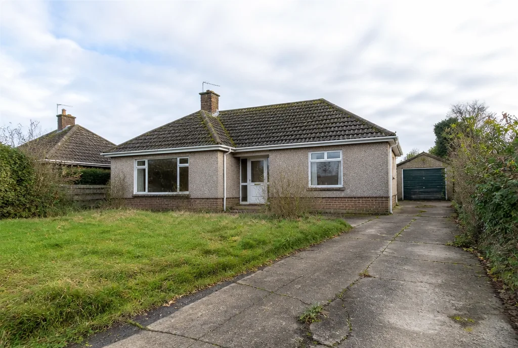 A 1960s bungalow with dated windows and an overgrown front garden, on a wide plot in a village