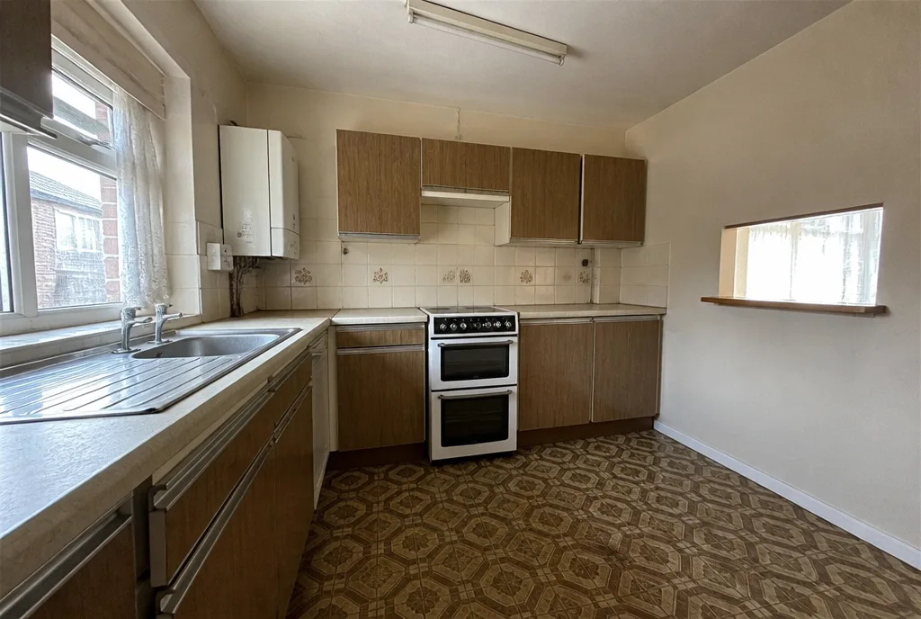 The dated kitchen of the Great Casterton bungalow with 1970s units and a serving hatch