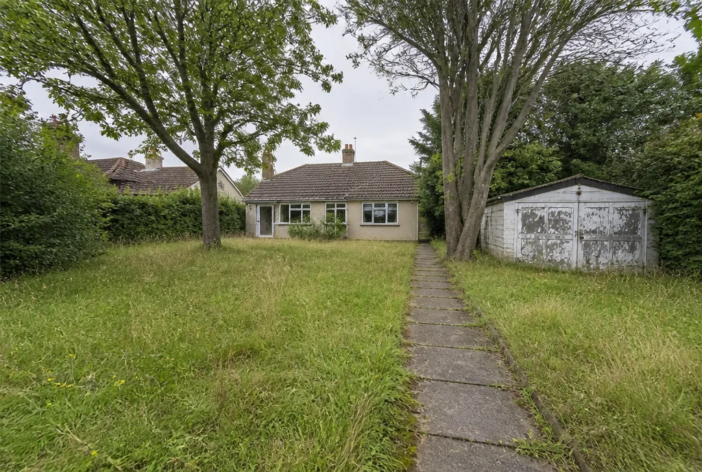 The large rear plot at Great Casterton, overgrown lawn with mature trees and a garage