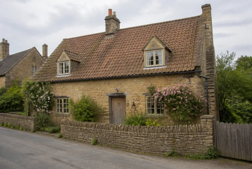 A honey-stone cottage with dormer windows and a low garden wall on Church Road in Ketton