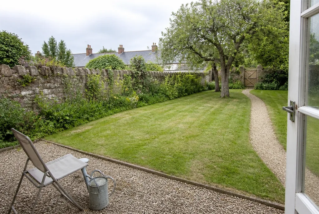 The rear garden at Ketton, lawn with a gravel path, apple tree and a stone boundary wall