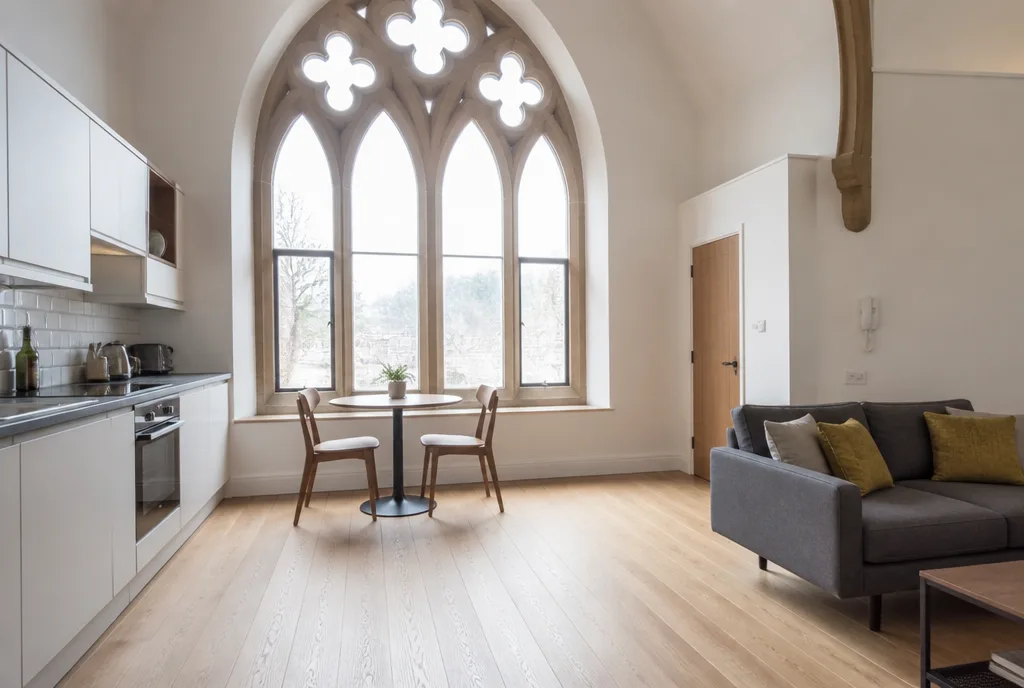 A top-floor apartment interior with a tall stone-mullioned arched window, white walls and pale oak floor