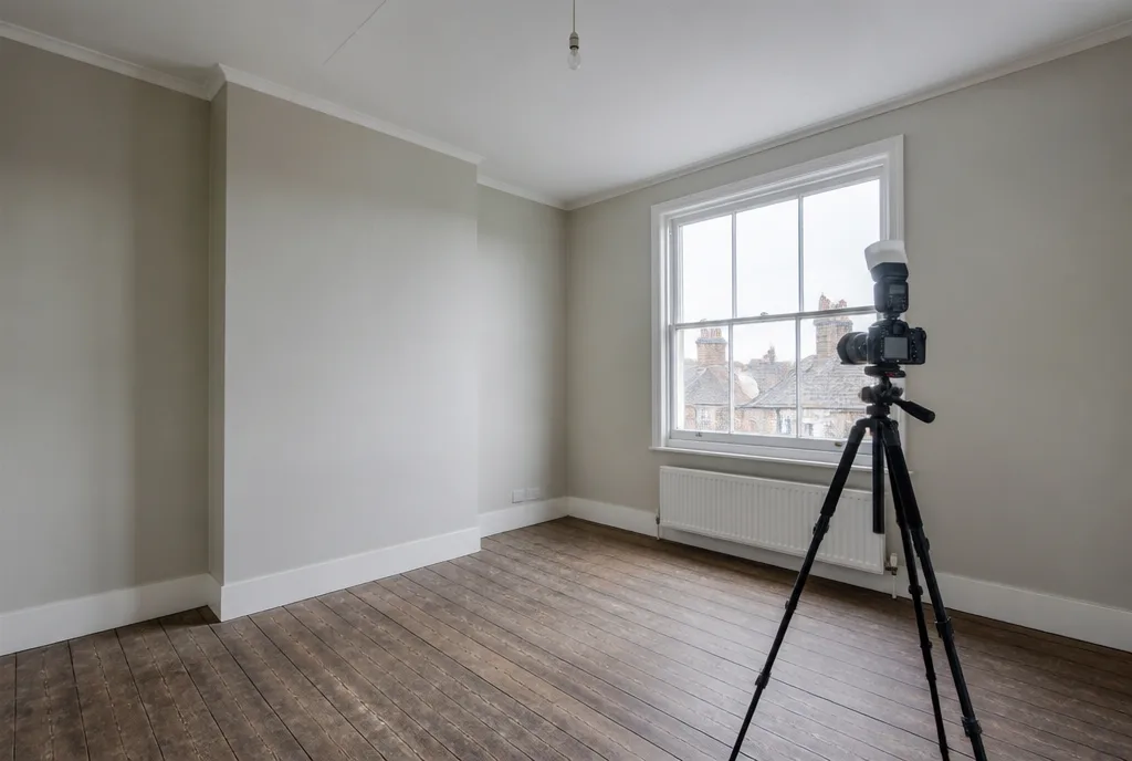 A camera on a tripod in an empty bedroom set up to photograph the window wall