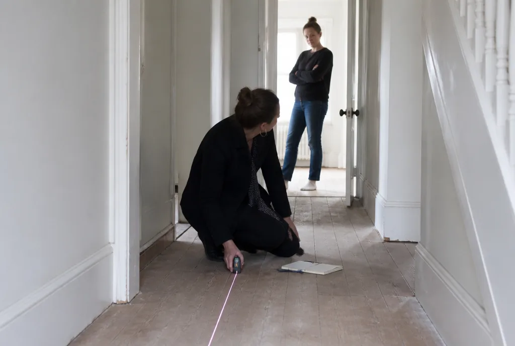 An agent kneeling in a hallway measuring the room with a laser measure while the owner watches