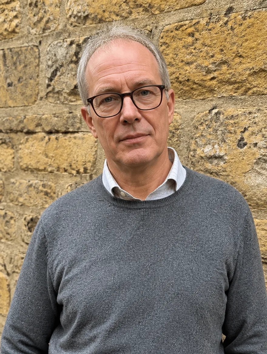 Tom Rook, co-founder of Welland & Rook, a man in his fifties with glasses and a grey wool jumper, photographed against a limestone wall
