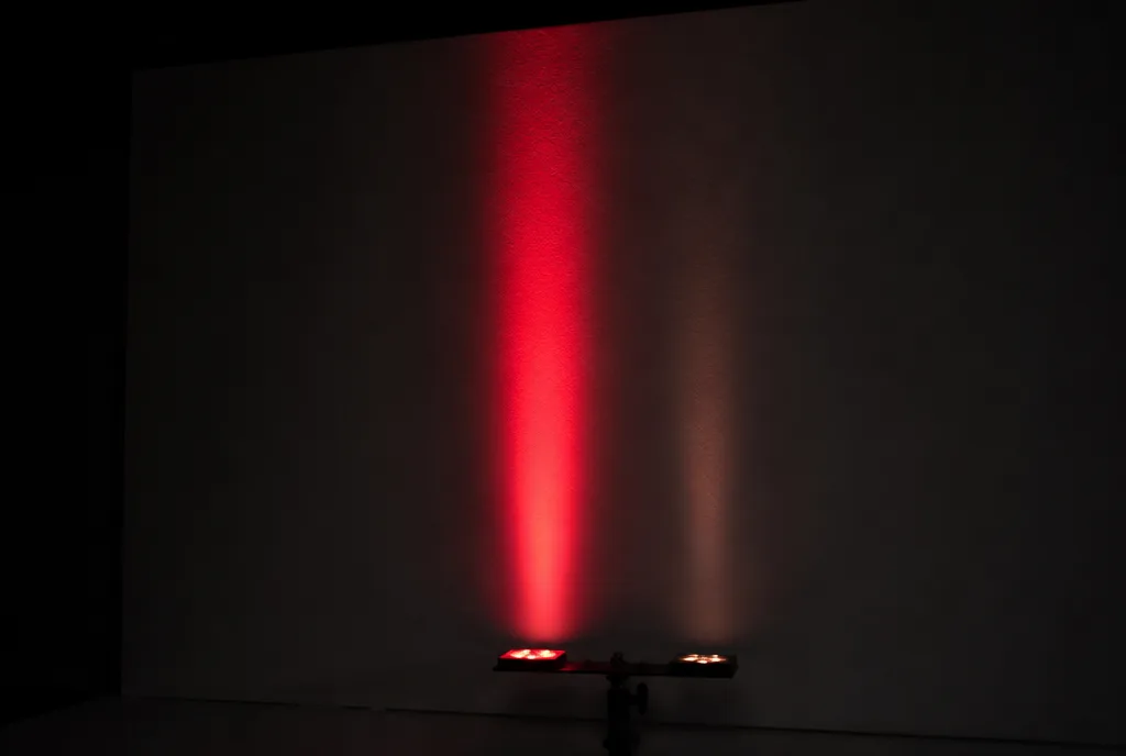 A visible red beam beside a faint near-infrared glow on a pale wall