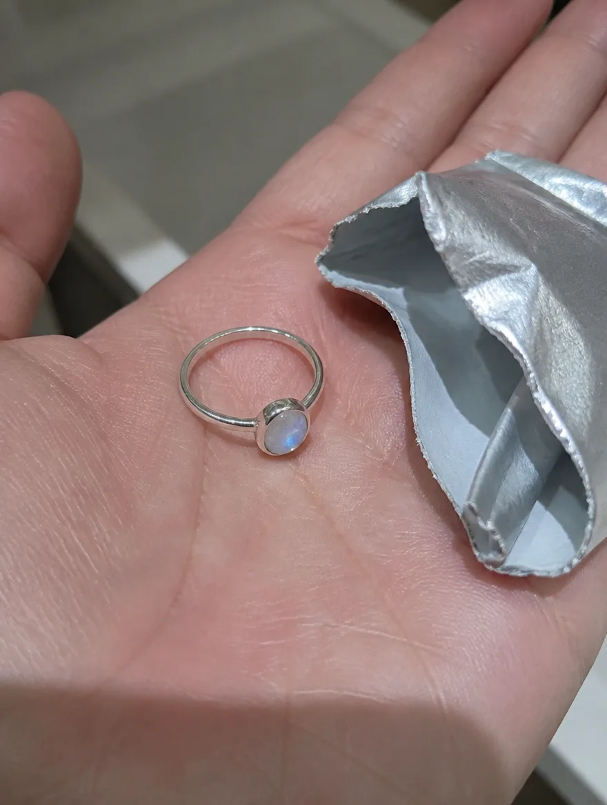 Moonstone oval ring in an open palm beside a torn foil pouch
