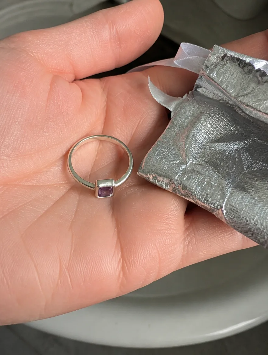 Amethyst square ring in an open palm beside a torn foil pouch