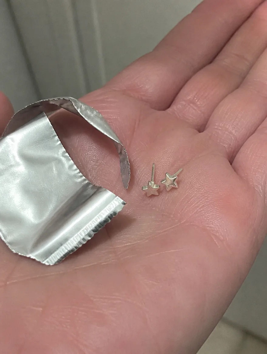 Star stud earrings in an open palm beside a torn foil pouch