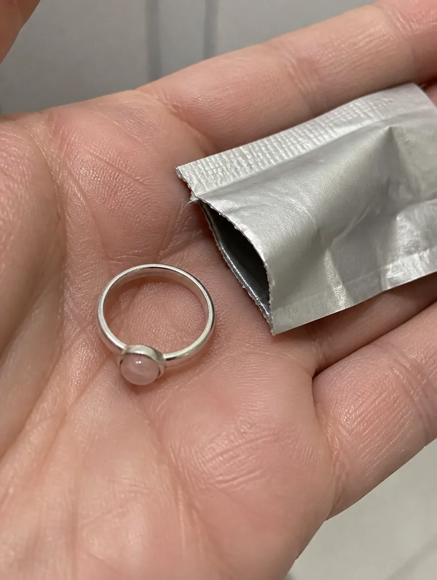 Rose quartz ring in an open palm beside a torn foil pouch