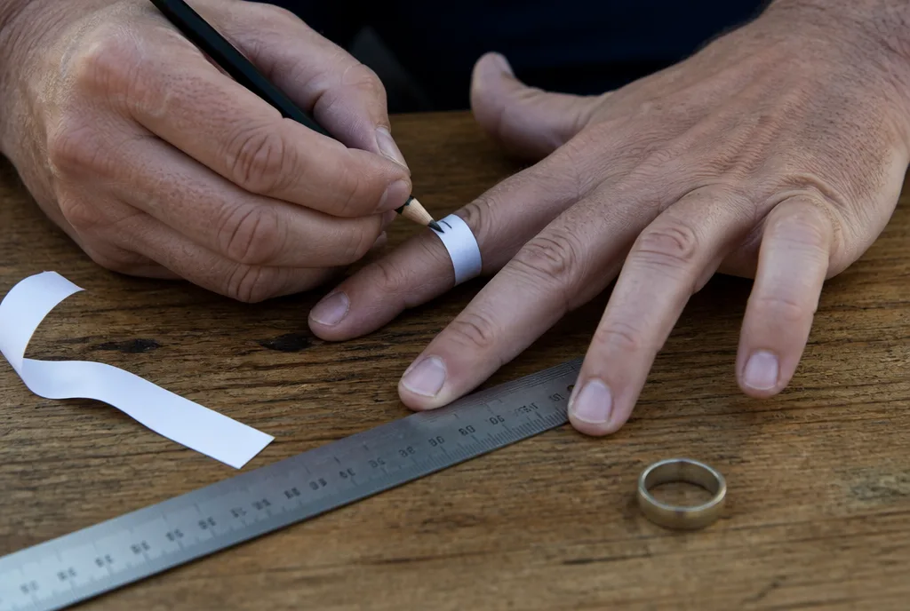 Hands measuring a ring finger with a strip of paper and a pencil