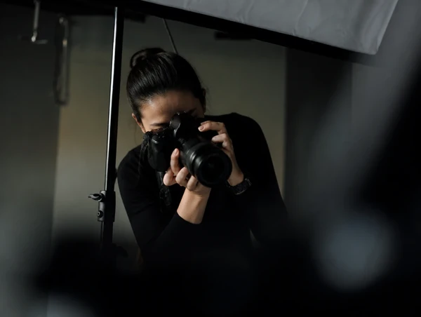 Chinese Malaysian woman photographer shoots with a DSLR in a dark studio beside a light stand